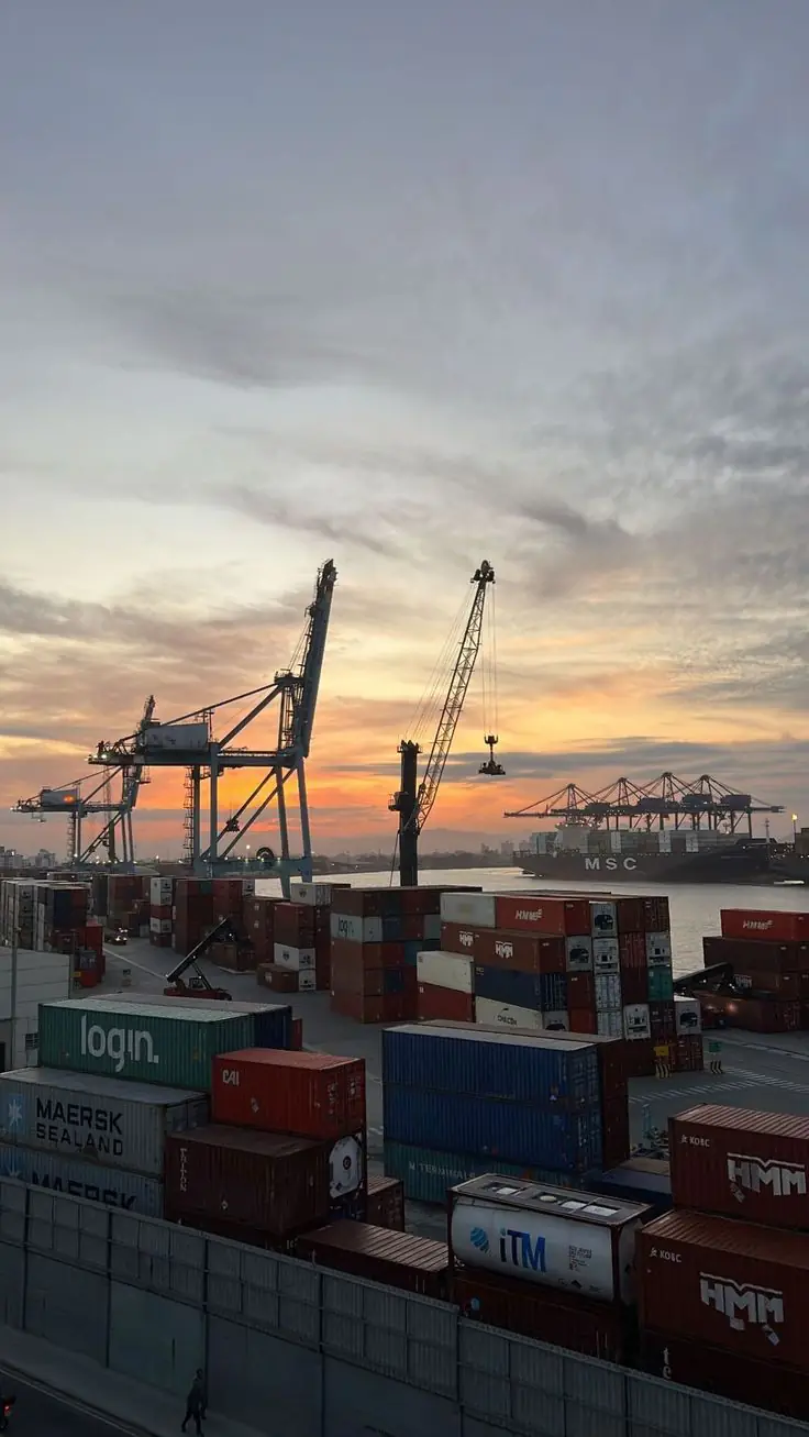Container port with cranes and stacked shipping containers at sunset